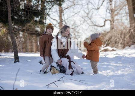 Eine aktive und fröhliche Mutter spaziert mit ihren kleinen Söhnen auf einem Pfad im Winterwald. Familienurlaub im Winter. Glückliche Mutterschaft. Stockfoto