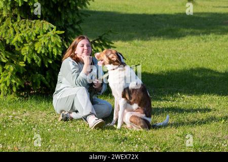 Eine Frau sitzt auf einer Wiese mit einem großen Hund im Sommer Russland Jaroslawl 10. August 2023 Stockfoto