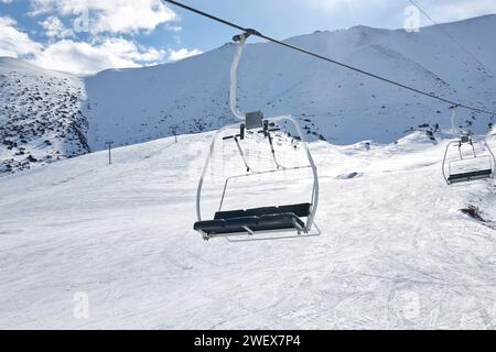 Seilbahnbau, leerer Dreisitzer-Sessel vor dem Hintergrund der verschneiten Berghänge, Skigebiet-Route. Winteraktivitäten, Skifahren, Snowboarden Stockfoto