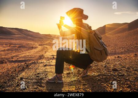 Eine junge Frau mit Rucksack sitzt und fotografiert die Wüste Gobi bei Sonnenuntergang Stockfoto