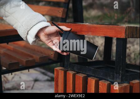 Frau Hand wirft einen recycelbaren Karton Kaffee in einen Mülleimer in einem Park Stockfoto