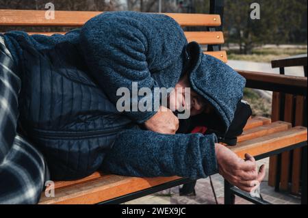 Obdachloser alter Mann liegt im Herbst auf einer Parkbank Stockfoto