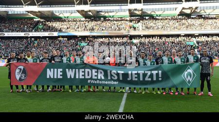 27. Januar 2024, Bremen: Fußball: Bundesliga, Werder Bremen - SC Freiburg, 19. Spieltag, wohninvest Weserstadion. Die Teams Werder Bremen und SC Freiburg stehen zusammen hinter einem Banner mit der Aufschrift „Never Again is now #WeRemember“. Am Tag des Gedenkens an die Opfer des Nationalsozialismus setzte der deutsche Profi-Fußball ein Zeichen gegen Antisemitismus. Bei Spielen in den Stadien, auf dem Trainingsplatz und bei anderen Veranstaltungen gedachten Vereine und Fans an die Verbrechen der NS-Zeit am Jahrestag der Befreiung des ehemaligen deutschen Konzentrationslagers Auschwitz. Foto: Carmen Jaspersen/dpa - Stockfoto