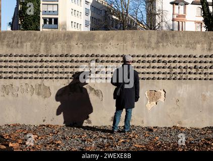 Frankfurt, Deutschland. Januar 2024. Ein Mann schaut auf die Mauer eines alten jüdischen Friedhofs an der Battonnstraße in Frankfurt, 27. Januar 2024. Im Jahr 2005 verabschiedete die UN-Generalversammlung eine Resolution, die den 27. Januar zum Internationalen Tag des Gedenkens an die Opfer des Holocaust erklärte, dem Tag, an dem das Vernichtungslager Auschwitz 1945 befreit wurde. Die Mauern der alten jüdischen Friedhöfe enthalten kleine Stahlblöcke, die die Namen der zwischen 1933 und 1945 deportierten und ermordeten Frankfurter Juden dokumentieren. Quelle: Zhang Fan/Xinhua/Alamy Live News Stockfoto