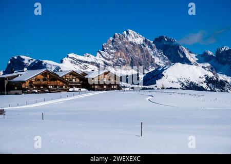 Hügelige Agrarlandschaft mit Alpenhotel Panorama und schneebedeckten Weiden auf der Seiser Alm, im Winter Gipfel der Geißler-Gruppe in der Ferne. Stockfoto