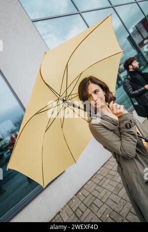 Stilvolle Frau mit gelbem Schirm auf der Stadtstraße an bewölktem Tag. Stockfoto