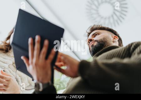 Low-View-Aufnahme eines männlichen Mitarbeiters, der ein Notizbuch hält und Projektdetails mit Kollegen diskutiert. Stockfoto