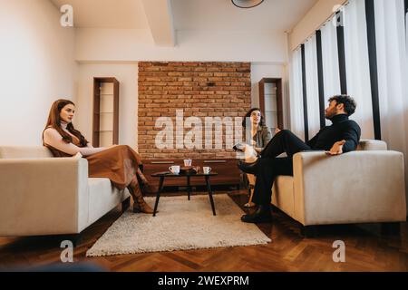 Zwangloses Geschäftstreffen mit drei Kollegen, bei dem die Arbeit in einem gemütlichen Wohnzimmer mit Backsteinmauern diskutiert wird Stockfoto