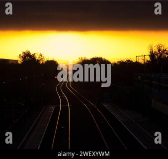 Sonnenaufgang am Bahnhof Bicester North auf der Hauptstrecke von Chiltern mit goldener Sonne, die von der Bahnstrecke mit farbigen Lichtsignalen strahlt. Stockfoto