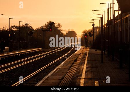 Sonnenaufgang am Bahnhof Bicester North auf der Hauptstrecke von Chiltern mit goldener Sonne, die von der Bahnstrecke mit farbigen Lichtsignalen strahlt. Stockfoto