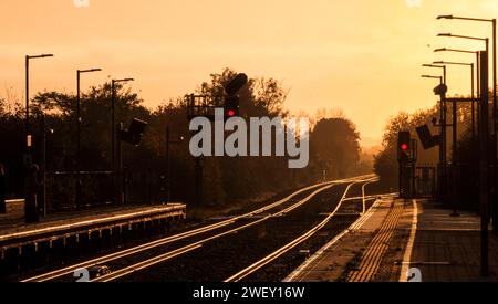 Sonnenaufgang am Bahnhof Bicester North auf der Hauptstrecke von Chiltern mit goldener Sonne, die von der Bahnstrecke mit farbigen Lichtsignalen strahlt. Stockfoto