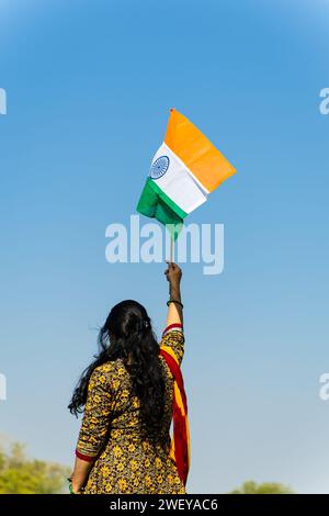 Ein junges indianermädchen, das die indische Nationalflagge hält und tagsüber mit hellblauem Himmel winkt Stockfoto