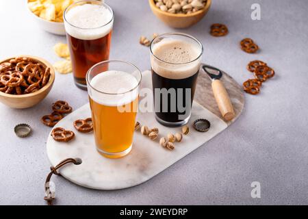 Dunkles Stout, Lager- und Ale-Bier in hohen Gläsern auf dem Tisch, verschiedene Biere mit Snacks, Brezeln und Pommes frites Stockfoto