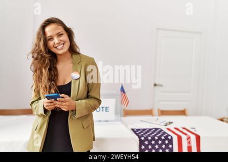 Junge schöne hispanische Frau Wahltisch Präsident mit Smartphone an Wahlhochschule Stockfoto