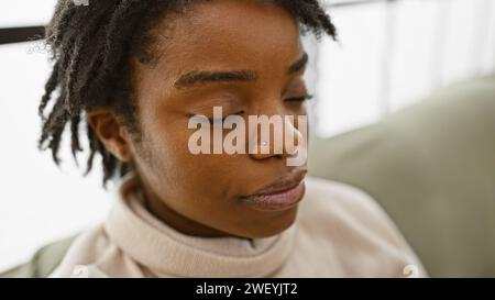 Junge afroamerikanische Frau mit Dreadlocks in einem neutralen Raum, die Augen geschlossen, die Ruhe reflektiert. Stockfoto