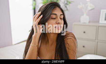 Eine ruhige südasiatische Frau genießt einen Moment der Ruhe in ihrem minimalistischen Schlafzimmer. Stockfoto