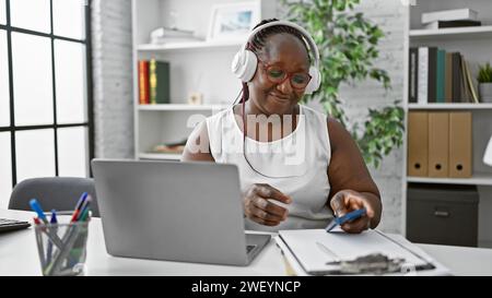 Lächelnde afroamerikanische Frau, Chef mit Zöpfen, Freude am Erfolg beim Tanzen, Musik am Telefon am Arbeitsplatz hören Stockfoto