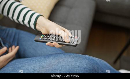 Nahaufnahme einer Frau, die sich zu Hause auf einem Sofa zurücklehnt und einen Knopf auf der Fernbedienung des fernsehers drückt. Stockfoto