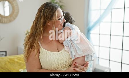 Glückliche Mutter steht zuversichtlich zu Hause, hält ihre liebenswerte Tochter in den Armen und genießt gemeinsam die Liebe der Familie in ihrem Wohnzimmer mit einem Stockfoto