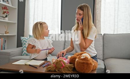 Entspannte Mutter-Tochter-Bindung, kaukasische Mutter und kleines Mädchen zeichnen auf dem Notebook und unterhalten sich zu Hause über das Smartphone ernsthaft Stockfoto