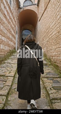 Rückansicht einer brünetten Frau, die durch eine gepflasterte Gasse in der historischen Umgebung des topkapi-Palastes in istanbul spaziert. Stockfoto