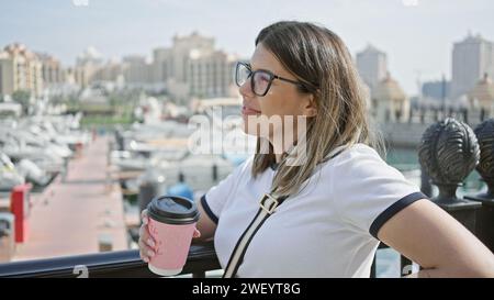 Eine junge Frau, die eine Tasse Kaffee hält, genießt einen ruhigen Blick auf die Skyline von doha mit eleganter Architektur und modernen Gebäuden. Stockfoto