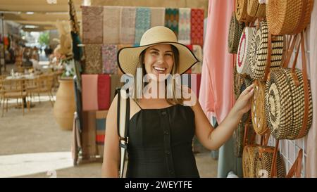 Lächelnde Frau in einem Sonnenhut, die einen traditionellen Markt in dubai erkundet und handgefertigte Taschen ansieht. Stockfoto