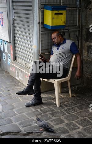 Port Louis, Mauritius - 25. Oktober 2023: Mann sitzt und schaut auf sein Telefon auf dem Central Market. Stockfoto