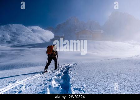 Ein Skitourengeher geht im Winter durch Nebel zur Berghütte Baita Segantini, die Gipfel der hellen Gruppe in der Ferne. San Martino di Castroz Stockfoto