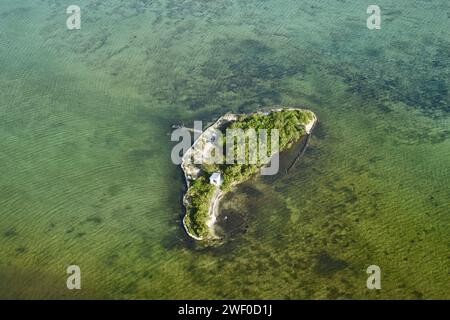 Eine kleine Insel mit einer Fischerhütte und zwei Piers, von einem Flugzeug aus gesehen, das über Belizean Gewässer fliegt. Stockfoto