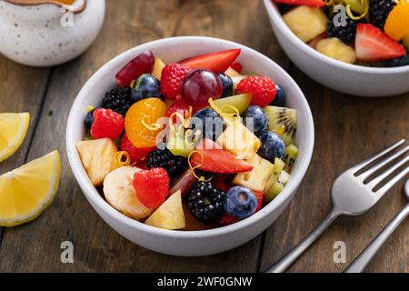 Gesunder und farbenfroher Obstsalat mit Banane, Ananas, Beeren, Orangendressing und frischer Minze Stockfoto
