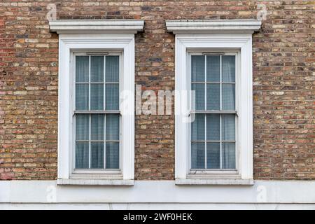 Zwei klassische weiße Fenster mit typischer londoner Architektur mit roter Backsteinmauer Stockfoto