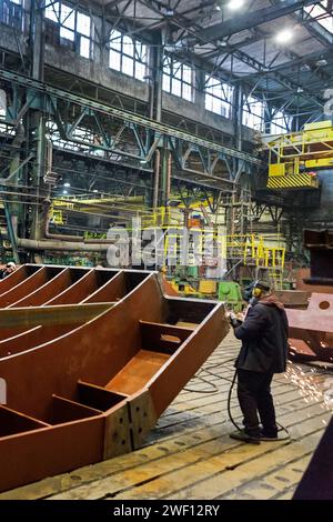 Der Arbeiter in einer Maske schleift ein Metallteil in einer Fabrik oder schneidet es mit einer elektrischen Kreissäge. Stockfoto