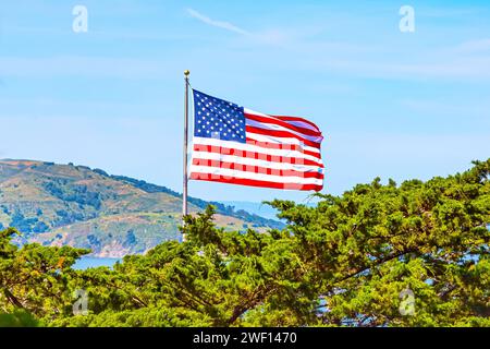 Amerikanische Flagge im Wind, Naturhintergrund mit Bergen und Bäumen. Amerikanische Flagge mit Blick auf die Berge amerikanische Flagge auf einem Hügel mit Blick auf Bäume und Berge. Amerikanische Flagge in San Francisco Stockfoto