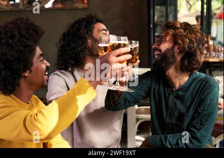 Eine kleine Gruppe von männlichen Freunden aus verschiedenen Rassen, die gemeinsam in einer Bar mit Bier trinken. Stockfoto