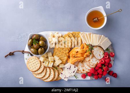 Kleiner Käse und Crackerbrett mit frischen Beeren und Oliven serviert mit Honig Stockfoto