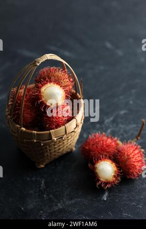 Frischer Rambutan, Sommerfrucht in einem Korb auf schwarzem Hintergrund. Beliebte Früchte aus Sout Ostasien Stockfoto