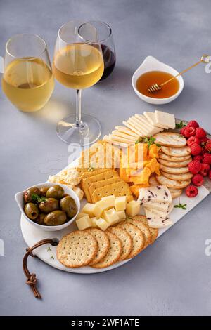 Kleiner Käse und Crackerbrett mit frischen Beeren und Oliven serviert mit Honig und mehreren Gläsern Wein Stockfoto