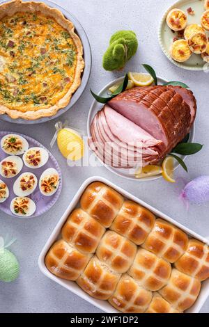 Osterbrunch auf einem großen Tisch mit spiralförmigem Schinken, Quiche, Eiern und heißen Kreuzbrötchen mit Osterdekor Stockfoto