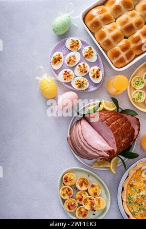 Osterbrunch auf einem großen Tisch mit spiralförmigem Schinken, Quiche, Eiern und heißen Kreuzbrötchen mit Osterdekor und Kopierraum Stockfoto
