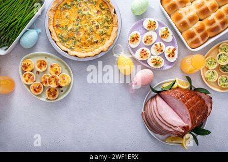Osterbrunch auf einem großen Tisch mit spiralförmigem Schinken, Quiche, Eiern und heißen Kreuzbrötchen mit Osterdekor und Kopierraum Stockfoto