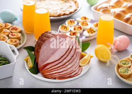 Osterbrunch auf einem großen Tisch mit spiralförmigem Schinken, Quiche, Eiern und heißen Kreuzbrötchen mit Osterdekor Stockfoto