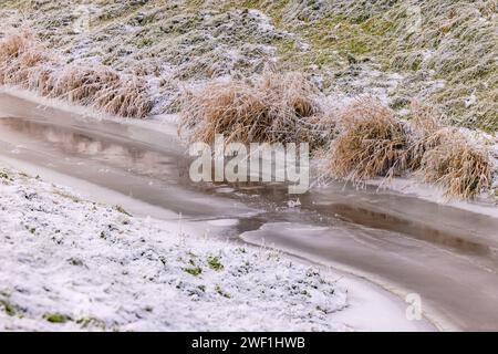 Im Winter gefrorener Bach mit Eis und Schnee auf einem Hang mit Gras Stockfoto
