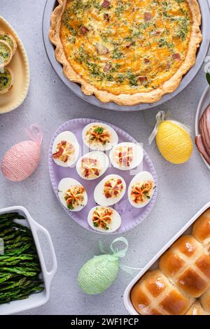 Osterbrunch auf einem großen Tisch mit spiralförmigem Schinken, Quiche, Eiern und heißen Kreuzbrötchen mit Osterdekor Stockfoto