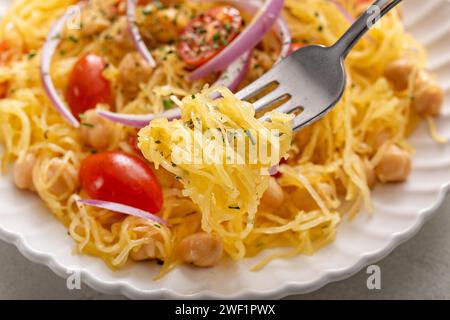Spaghetti-Kürbis mit Kichererbsen und Tomaten, garniert mit roten Zwiebeln, kohlenhydratarmen und veganen Rezeptideen, mit einer Gabel Stockfoto
