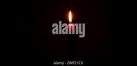Eine einzelne brennende Kerzenflamme oder Licht leuchtet auf roter Kerze auf schwarzem oder dunklem Hintergrund auf dem Tisch in der Kirche zu Weihnachten, Beerdigung oder Gedenkfeier Stockfoto