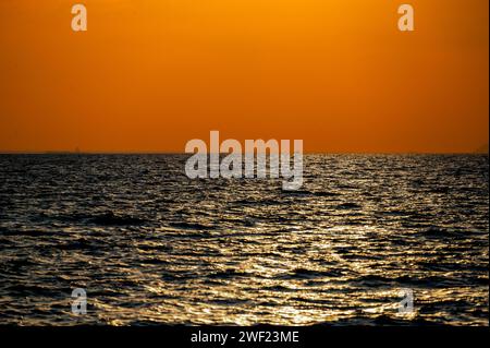 Feuriger Sonnenuntergang über dem Ozean, mit leuchtenden Orange- und Rottönen am Himmel. Die Sonne geht dramatisch unter, wirft warmes Licht auf dunkles Wasser unter und erzeugt B Stockfoto