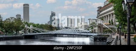 Singapur, 24. Januar 2024: Die Cavenagh Bridge erstreckt sich elegant über den Singapore River, das berühmte Fullerton Hotel und die majestätischen Wolkenkratzer. Architektonisch Stockfoto