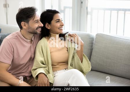Glückliches, nachdenkliches lateinamerikanisches Ehepaar, das auf der Heimcouch sitzt Stockfoto