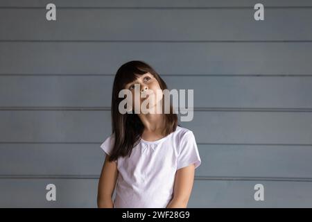 Träumendes kleines Mädchen, das an der grauen Wand steht und sich vorstellt Stockfoto